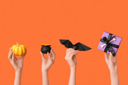 Female hands with pumpkin, pot, paper bat and gift box on orange background. Halloween celebration