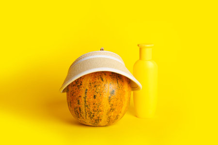 Pumpkin with hat and sunscreen cream on yellow background