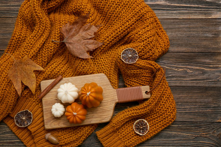 Composition with candles in shape of pumpkins, stylish warm sweater and fallen leaves on wooden backgroundの写真素材