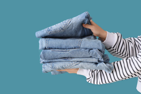 Female hands with stack of stylish jeans on blue background, closeupの写真素材