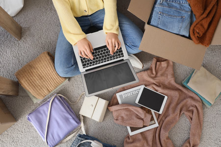 Young woman with laptop and stacks of clean clothes at homeの写真素材