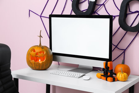 Workplace with modern computer, web and pumpkins in office interior decorated for Halloween celebrationの写真素材