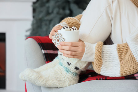 Woman in warm Christmas socks with cup of cocoa in armchair at home, closeupの写真素材