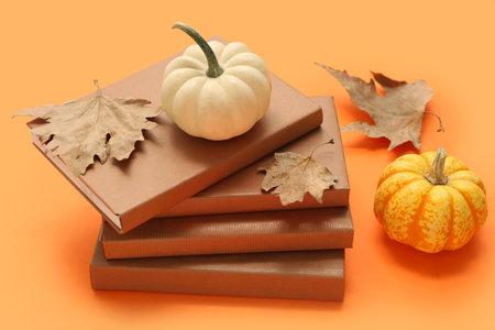 Stack of books, pumpkins and maple leaves on color backgroundの写真素材