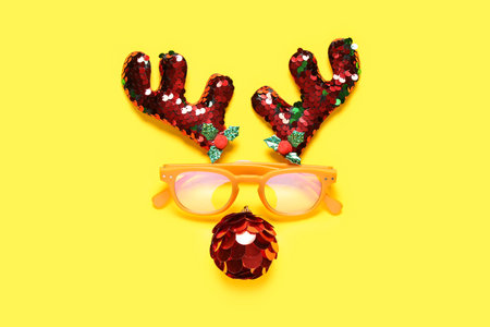 Reindeer face made of horns with eyeglasses and Christmas ball on yellow backgroundの写真素材