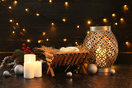 Manger with baby, fir branches, burning candles and glowing lights on dark background. Christmas...