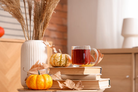 Glass cup of hot tea with pumpkins, books and autumn leaves on table in roomの写真素材