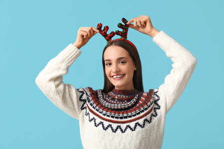 Young woman in sweater with Christmas reindeer horns on blue backgroundの写真素材