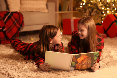 Cute happy little girls in checkered pajamas with book reading Christmas story at nightの写真素材