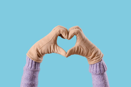 Woman in warm gloves making heart gesture on blue backgroundの写真素材