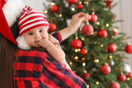 Happy mother in Santa hat with her little baby decorating Christmas tree at home, closeupの写真素材