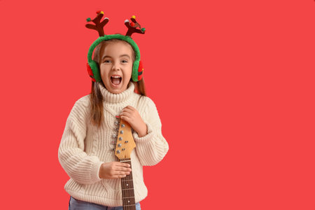Cute little girl in Christmas reindeer horns with guitar on red backgroundの写真素材