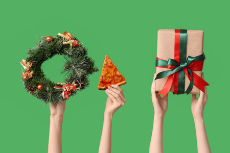 Female hands with pizza slice, wreath and gift box on green backgroundの写真素材