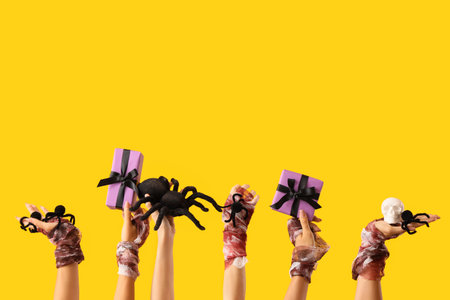 Female bandaged hands with Halloween gifts, skull and spiders on yellow backgroundの写真素材