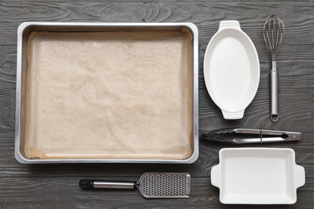 Composition with baking tray, ceramic dishes and kitchen utensils on dark wooden background