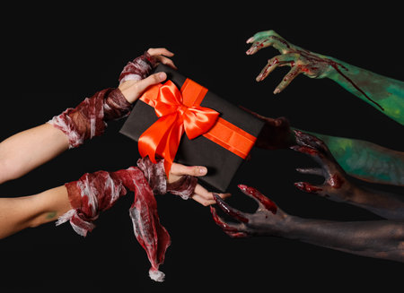 Painted female hands with Halloween gift on black background