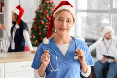 Mature female doctor in Santa hat with stethoscope at hospital on Christmas Eveの写真素材