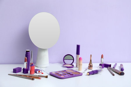 Different decorative cosmetics, makeup brushes and mirror on table near lilac backgroundの写真素材