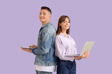 Young couple using laptops on lilac background