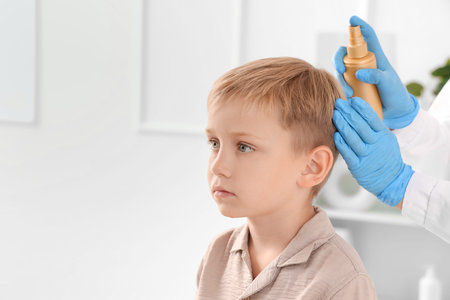 Female doctor spraying little boy's hair with pediculosis in clinic, closeup