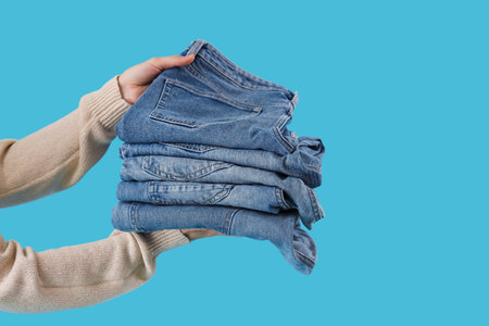 Female hands with stack of stylish jeans on blue background, closeupの写真素材