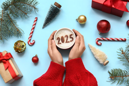 Woman holding cup of coffee with figure 2025, Christmas gifts and decorations on color background, closeupの写真素材