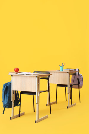 School desks with stationery and backpacks on yellow backgroundの写真素材