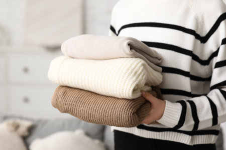 Young woman with stack of warm sweaters at home, closeupの写真素材
