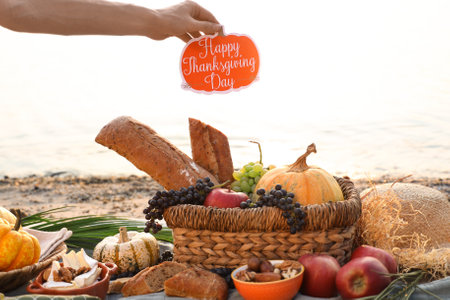 Woman having picnic with pumpkins, delicious food and Thanksgiving Day greeting card on beachの写真素材