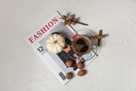 Cup of tasty pumpkin coffee with autumn decorations and magazine on grunge white backgroundの写真素材