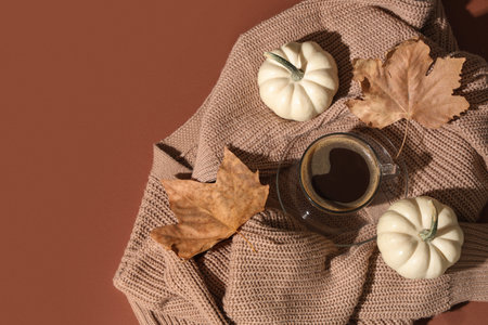 Cup of tasty pumpkin coffee with autumn decorations and warm sweater on brown backgroundの写真素材
