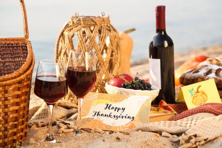 Delicious food, wine and greeting card with text HAPPY THANKSGIVING on beachの写真素材