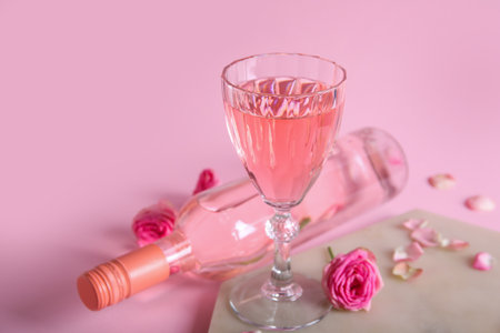 Glass and bottle of tasty pink wine with beautiful roses on color backgroundの写真素材