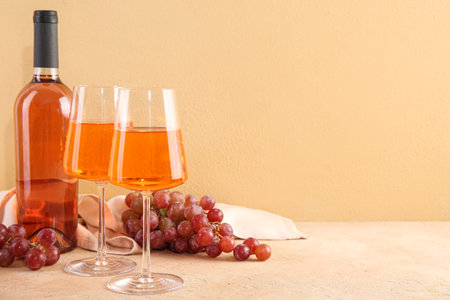 Glasses and bottle of tasty pink wine with fresh grapes on beige backgroundの写真素材