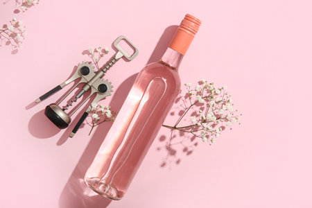 Bottle of tasty pink wine with opener and beautiful gypsophila flowers on color backgroundの写真素材