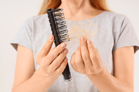 Mature woman with hair loss problem and brush on light background, closeupの写真素材