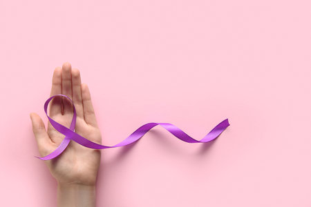 Female hand with purple ribbon on pink background. World Cancer Dayの写真素材