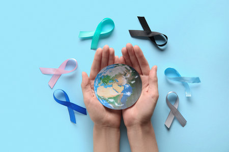 Female hands with colorful ribbons and paper planet Earth on blue background. World Cancer Dayの写真素材