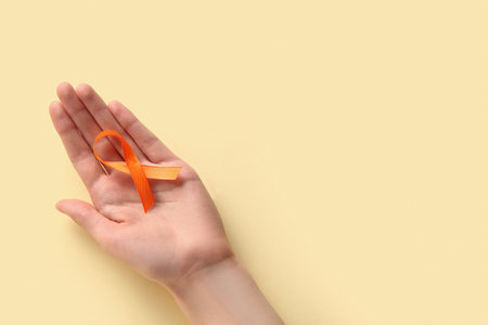 Female hand with orange ribbon on yellow background. World Cancer Dayの写真素材