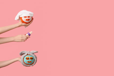 Women holding funny pumpkins with cosmetic masks and highlighter on pink backgroundの写真素材