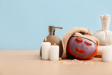 Funny pumpkin with false eyelashes, spa supplies and burning candles on color tableの写真素材