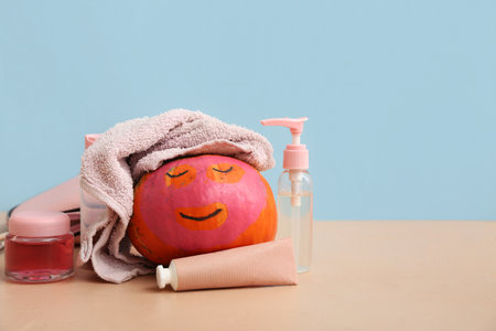 Funny pumpkin with drawn face, facial mask and cosmetic products on color tableの写真素材