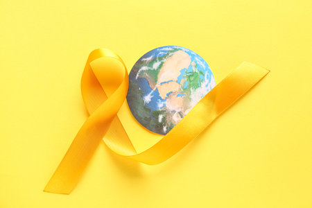 Yellow ribbon and paper planet Earth on color background. World Cancer Dayの写真素材