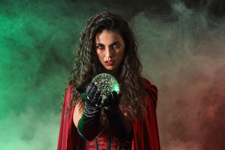 Young witch with crystal ball and smoke on dark background