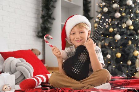 Cute little boy with candy cane and ukulele in bedroom on Christmas Eveの写真素材