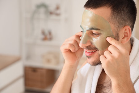 Handsome young happy man applying cosmetic gel mask on face in bathroom at homeの写真素材