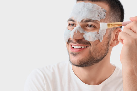 Handsome young happy man applying cosmetic bubble mask on face against gray backgroundの写真素材