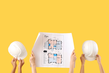 Architects with house plan and hardhats on yellow background