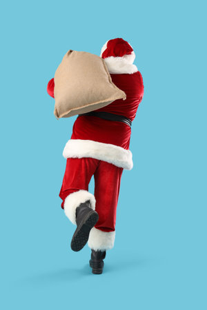 Santa Claus with Christmas bag running on blue background, back viewの写真素材