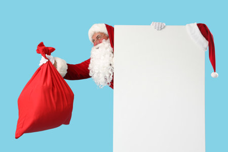 Santa Claus with Christmas bag and blank poster on blue backgroundの写真素材